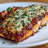 Keto Garlic Parmesan Salmon with Roasted Broccoli and Lemon Wedges served on a baking sheet, golden crust glistening with herbs and garlic.